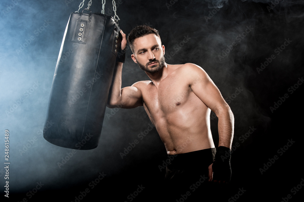 thoghtful athletic boxer holding punching bag on black with smoke thoghtful athletic boxer holding punching bag on black with smoke