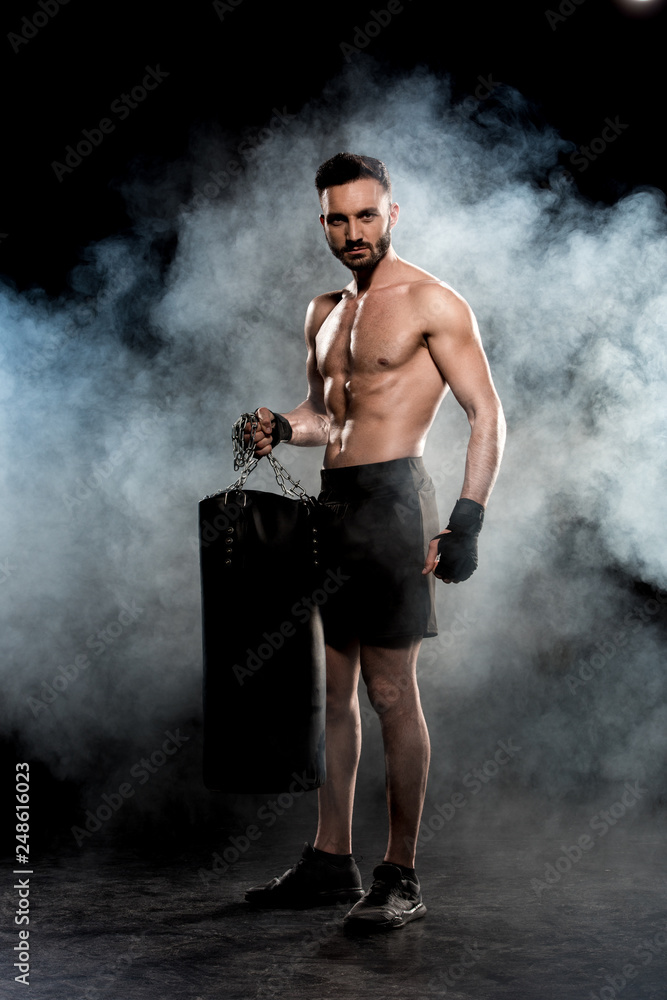 handsome boxer holding punching bag on black with smoke