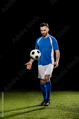 bearded sportsman in uniform training with ball on grass isolated on black © LIGHTFIELD STUDIOS