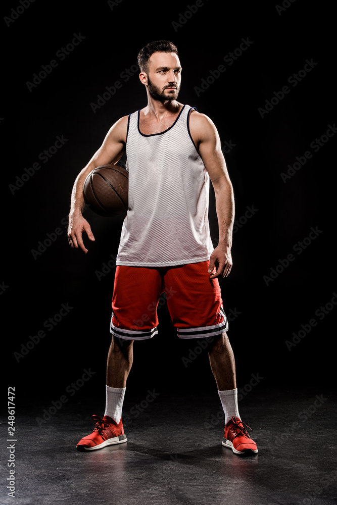 muscular basketball player standing with ball on black background
