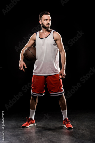 muscular basketball player standing with ball on black background © LIGHTFIELD STUDIOS