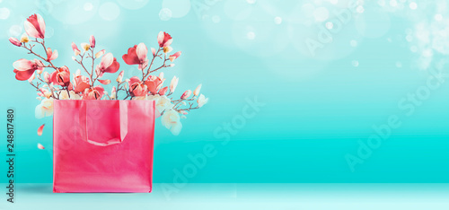 Shopping bag with pink spring blossom bunch standing at turquoise blue background. Trendy color. Creative spring time and summer concept. Magnolia blooming. Promotion and sale. Template or banner