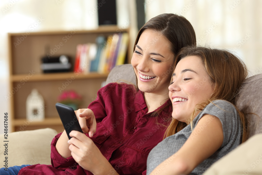 Two happy roommates checking smart phone content at home Two happy roommates checking smart phone content at home