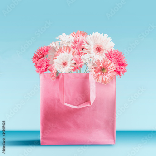 Pastel pink shopping bag with gerbera daisies flowers bunch standing on table at turquoise blue wall background. Branding mock up. Copy space. Summer love, sale and promotion concept © VICUSCHKA