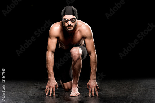 athletic swimmer standing in start position on black background