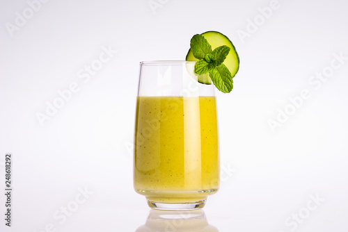 glass of green and yellow organic vegetable juice with slice of cucumber and mint leaf on white background