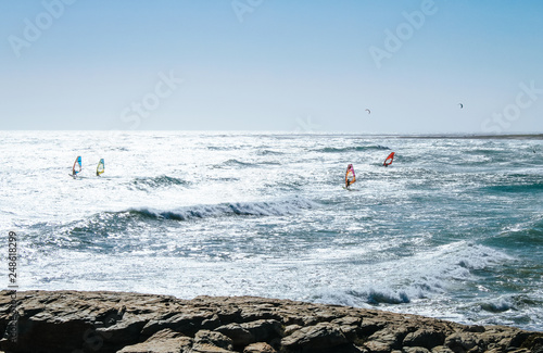 A group of Windsurfers riding the blue waves of a beach in the Cape of good hope National Park near Cape Town, South Africa