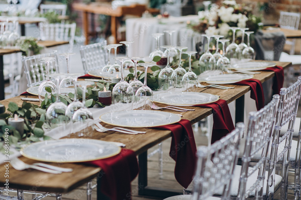 in the wedding banquet area there are tables and transparent chairs, on the tables there are plates, glasses, cutlery and compositions from green branches and candles in the wedding banquet area there are tables and transparent chairs, on the tables there are plates, glasses, cutlery and compositions from green branches and candles