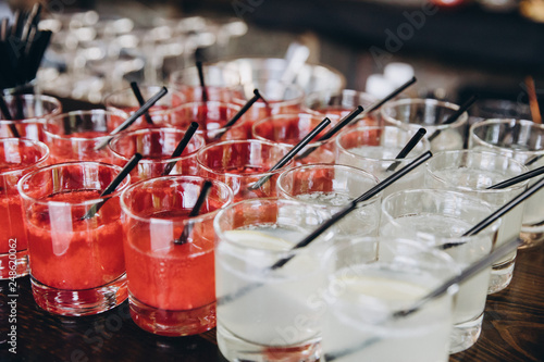 on the bar stand are glasses with white and red cocktails, straws in glasses