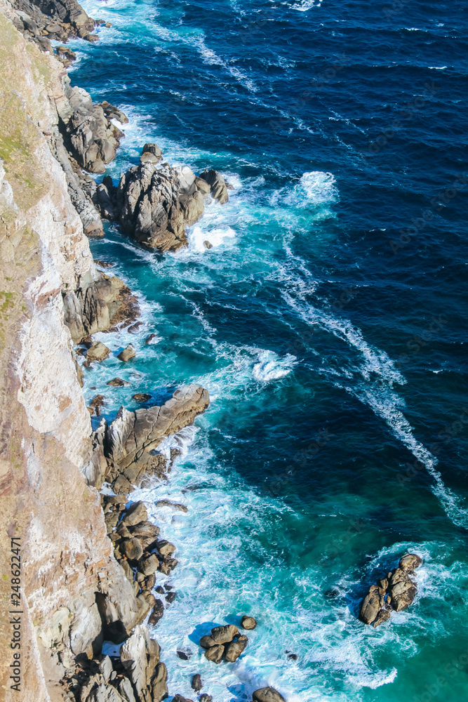 Background texture of a rocky shore and blue and turquoise water and waves of the Atlantic Ocean at the Cape of Good Hope in South Africa