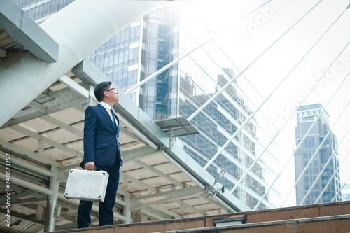 An Asian businessman holding a bag looking up at a tall building. Have space to write text