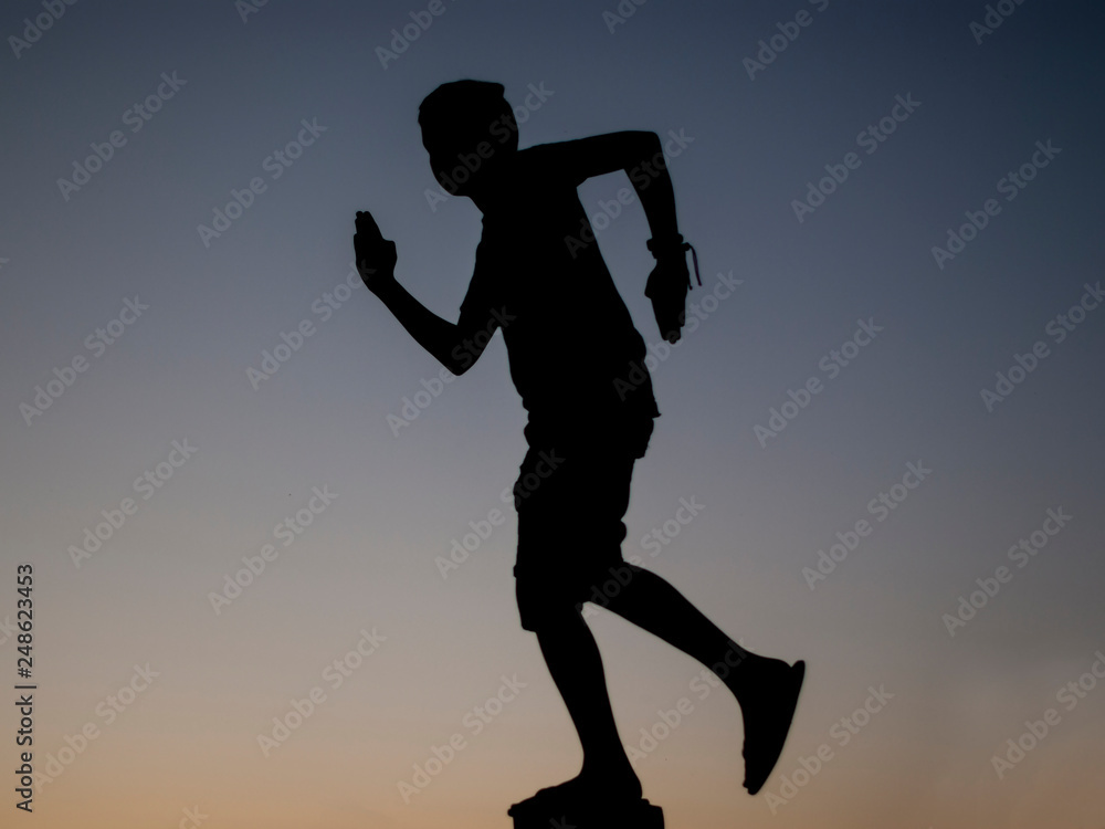 silhouette of a person boy running towards sunset sky background. Man in shorts and tank top silhouette.