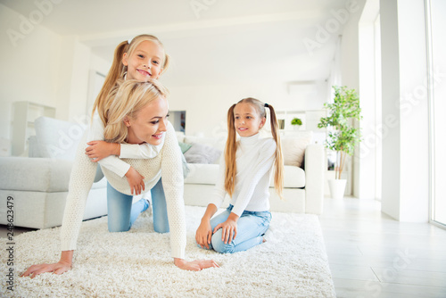 Nice cute lovely lovable fascinating dreamy sweet attractive cheerful cheery mama on carpet carrying piggybacking pre-teen girls spending free time having fun in light white room