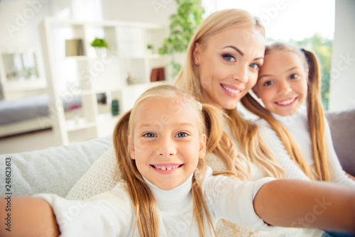 Self-portrait of nice adorable cute attractive lovely winsome charming people mom mum girls sitting on divan vacation in light white interior room hotel indoors