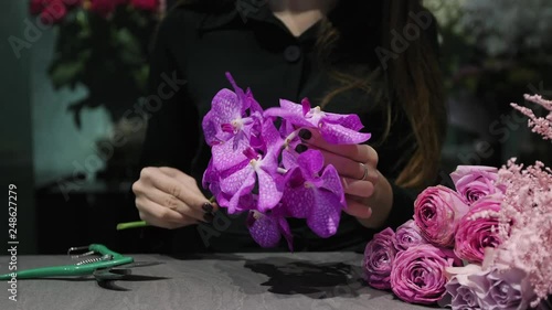 Professional woman florist makes the bouquet from pink flowers tulips, roses, orchids and solidago.