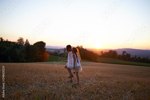 Beautiful classic shot of two cute Asian girls in white dresses walking across a field in the hills in summer sunset
