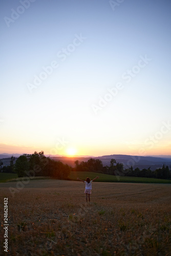 Beautiful classic shot of a little girl in a white dress walking on the hills of a field in spring sunset