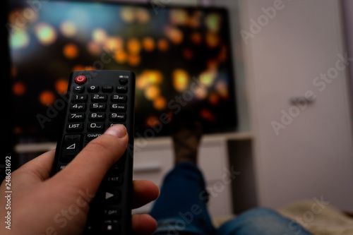 Female holding TV remote control in front of TV. Couch potatoe. Point of view shot.