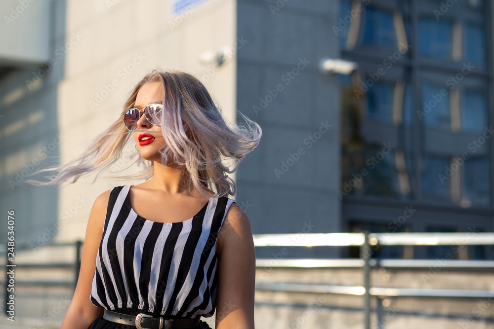 Adorable blonde model wearing glasses, posing with fluttering hair at the city. Space for text