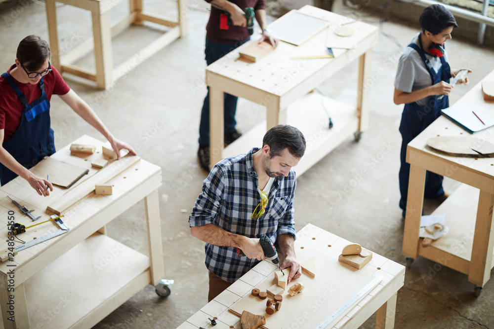 High angle view of busy carpenters standing at tables and working with ...