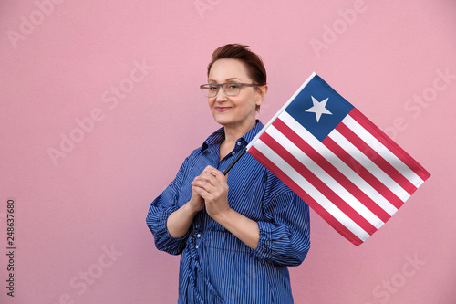 Liberia flag. Woman holding  Liberia flag. Nice portrait of middle aged lady 40 50 years old holding a large flag over pink wall background on the street outdoor. © theartofpics