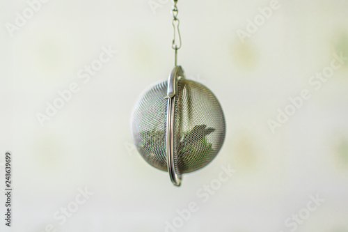 Cuadro en lienzo Suspended metal tea infuser with dried leaves of green tea and mint on clean bac