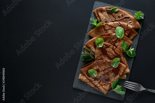 Homemade chocolate crepes served with blueberries, sauce and mint leaves on slate plate. Selective focus. Top view. Copy space photo