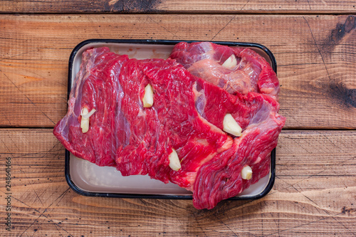 Raw beef for roasting with garlic on a wooden table, top view photo