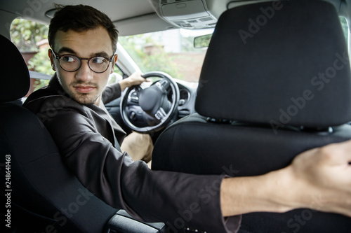 Young taxi driver looks back over the seats. He is sitting at his car.