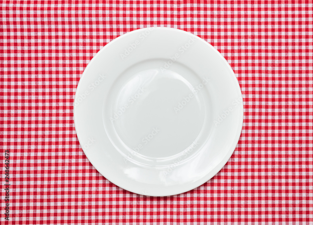 Empty white plate on red checkered tablecloth background Empty white plate on red checkered tablecloth background