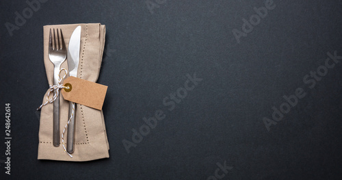 Table place setting with linen napkin and blank tag on black color background, banner