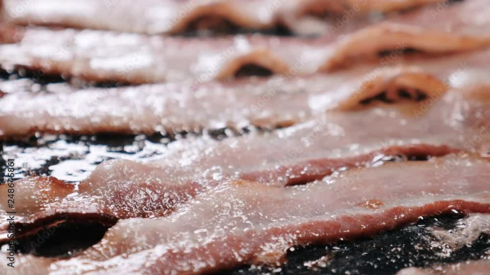 Close up roasted and crispy bacon slices on a stove. The camera is slowly moving in a clockwise direction over a close-up view of cooked, crispy, roasted bacon slices with bubbly cooking oil. Close up roasted and crispy bacon slices on a stove. The camera is slowly moving in a clockwise direction over a close-up view of cooked, crispy, roasted bacon slices with bubbly cooking oil.