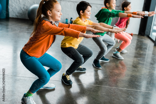 Preteen kids doing squats in gym together