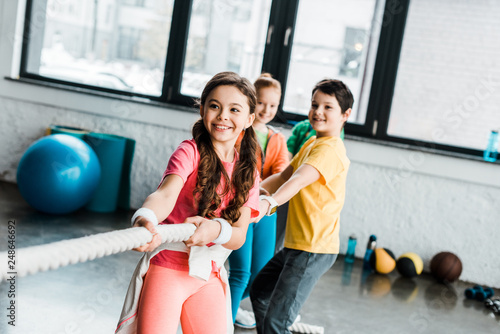 Smiling kids in sportswear pulling rope in gym