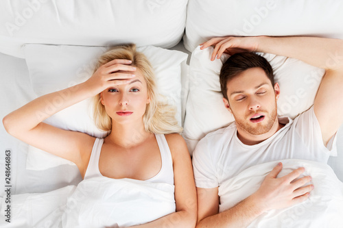 sleeping problems and people concept - unhappy woman lying in bed with snoring man photo