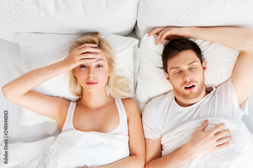 sleeping problems and people concept - unhappy woman lying in bed with snoring man