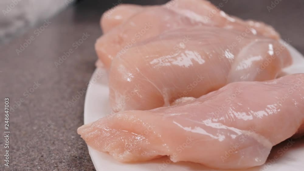 Fresh chicken fillet pieces. The video shows a hand placing uncooked fresh chicken fillet piece on a white plate. Fresh chicken fillet pieces. The video shows a hand placing uncooked fresh chicken fillet piece on a white plate.