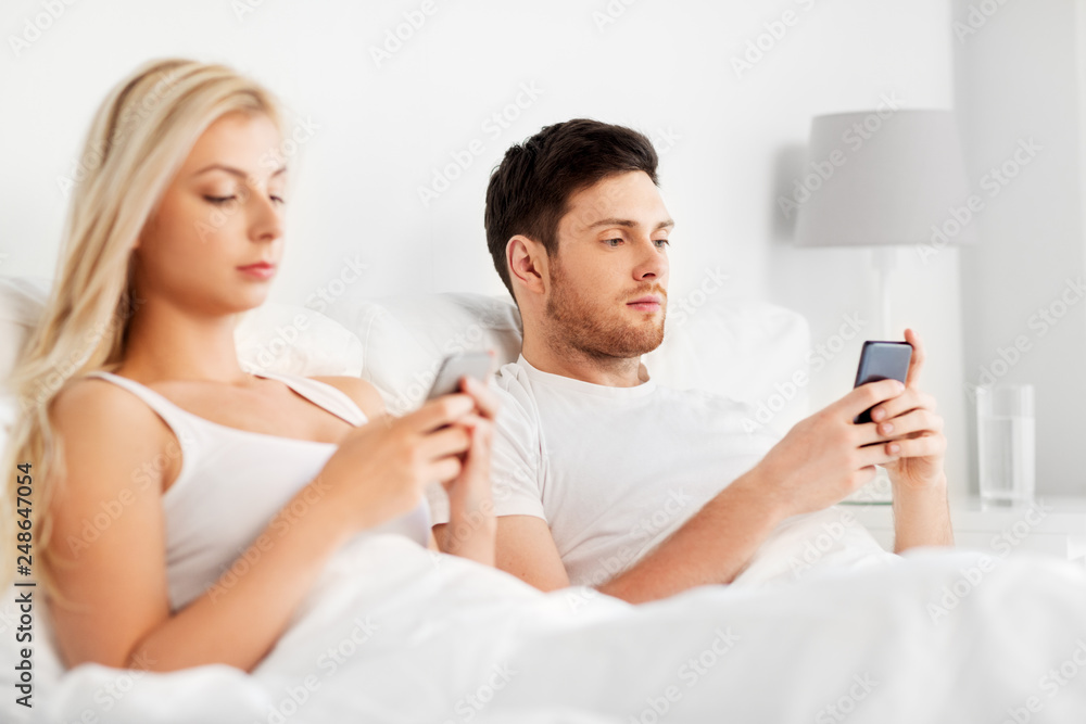 people, technology, internet addiction and communication concept - couple with smartphones in bed people, technology, internet addiction and communication concept - couple with smartphones in bed