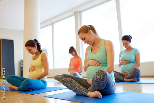 pregnancy, fitness and healthy lifestyle concept - group of happy pregnant women exercising in lotus pose at gym yoga