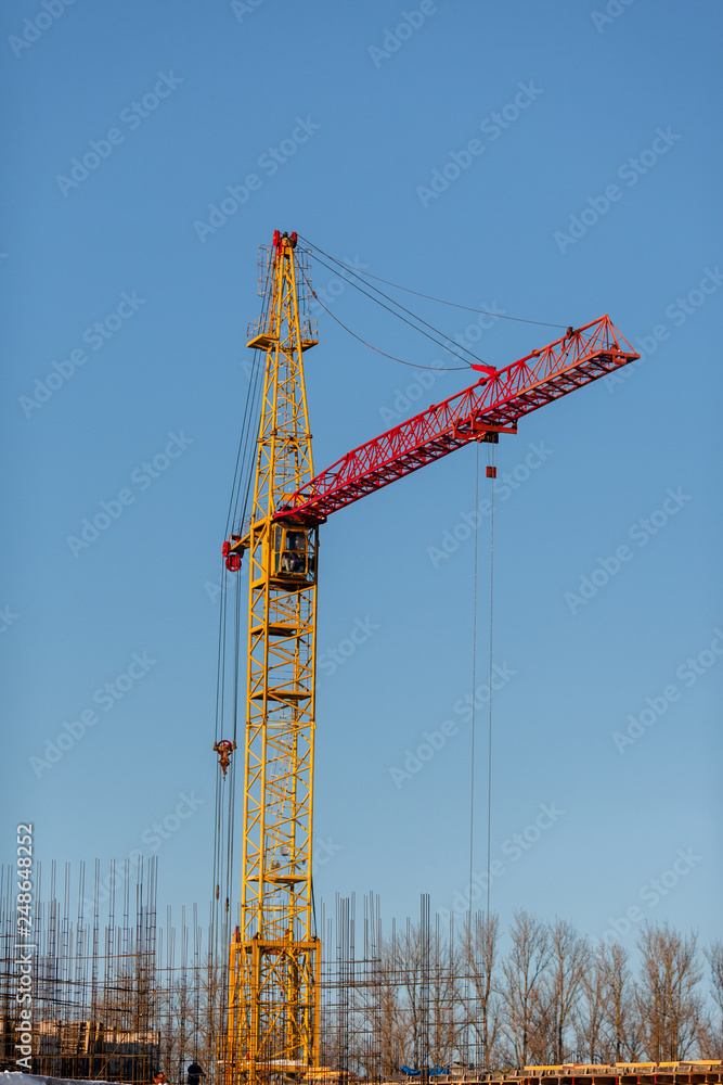 The yellow crane in the daylight. Construction technology. Modern construction crane for lifting building materials,on the background of home fittings