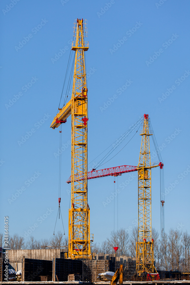 two yellow construction cranes raise-lower concrete slabs. Safety at the construction site, hard work of workers, modern technology for the rapid construction of buildings