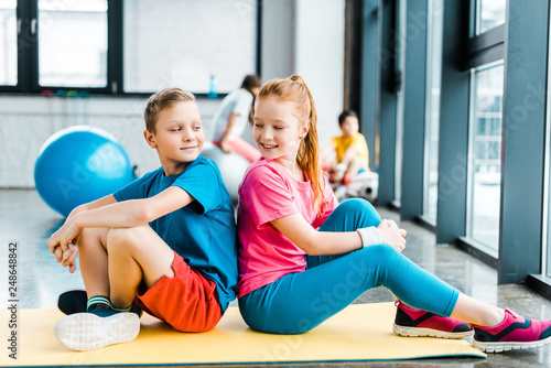 Two kids sitting back to back on fitness mat