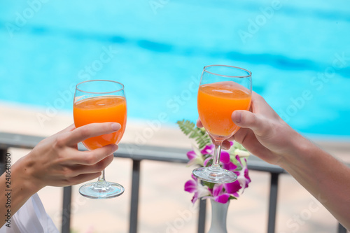 Happy couple with two glasses of orange juice at swiming pool vacation