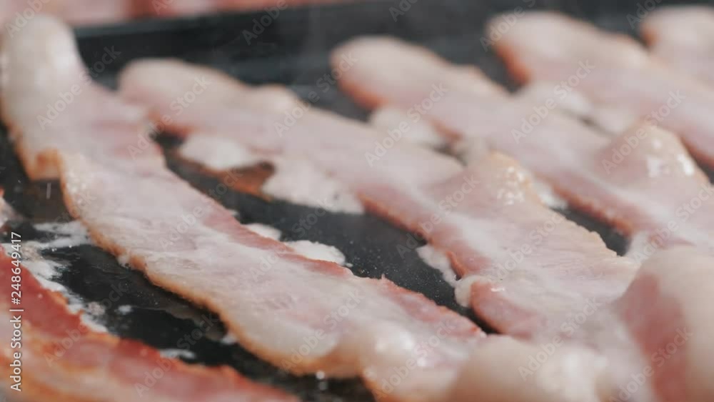 Strips of bacon on the stove, slide camera movement, close up shot. Close up panning shot of cooked, crispy, roasted bacon slices with bubbly cooking oil on a stove. Strips of bacon on the stove, slide camera movement, close up shot. Close up panning shot of cooked, crispy, roasted bacon slices with bubbly cooking oil on a stove.