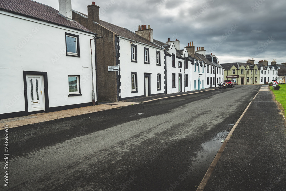 Narrow street in the small town. Northern Ireland. Amazing city scape the cottages in traditional Irish style. Grey cloudy sky before the rain. Attractive tourist destination. Narrow street in the small town. Northern Ireland. Amazing city scape the cottages in traditional Irish style. Grey cloudy sky before the rain. Attractive tourist destination.
