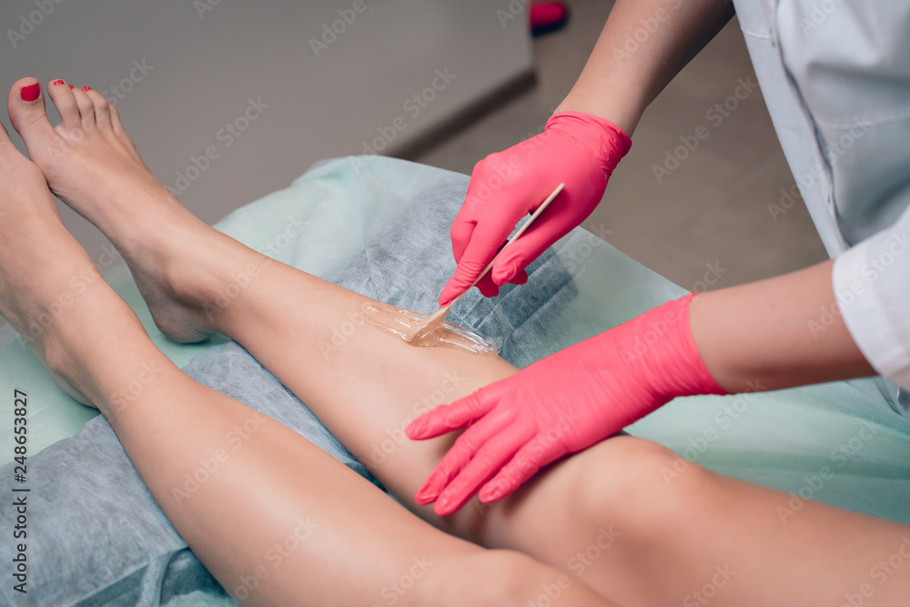 Fototapeta premium Beautician removes hair from a woman's legs. Sugaring. Hair removal with a special sugar paste has many advantages over wax depilation. Close-up..