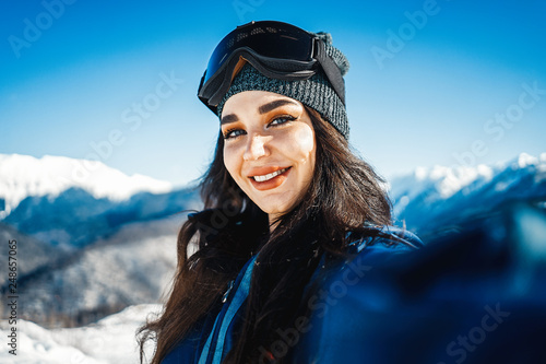 Attractive snowboard girl smiling and making selfie on mountain background. © Akaberka