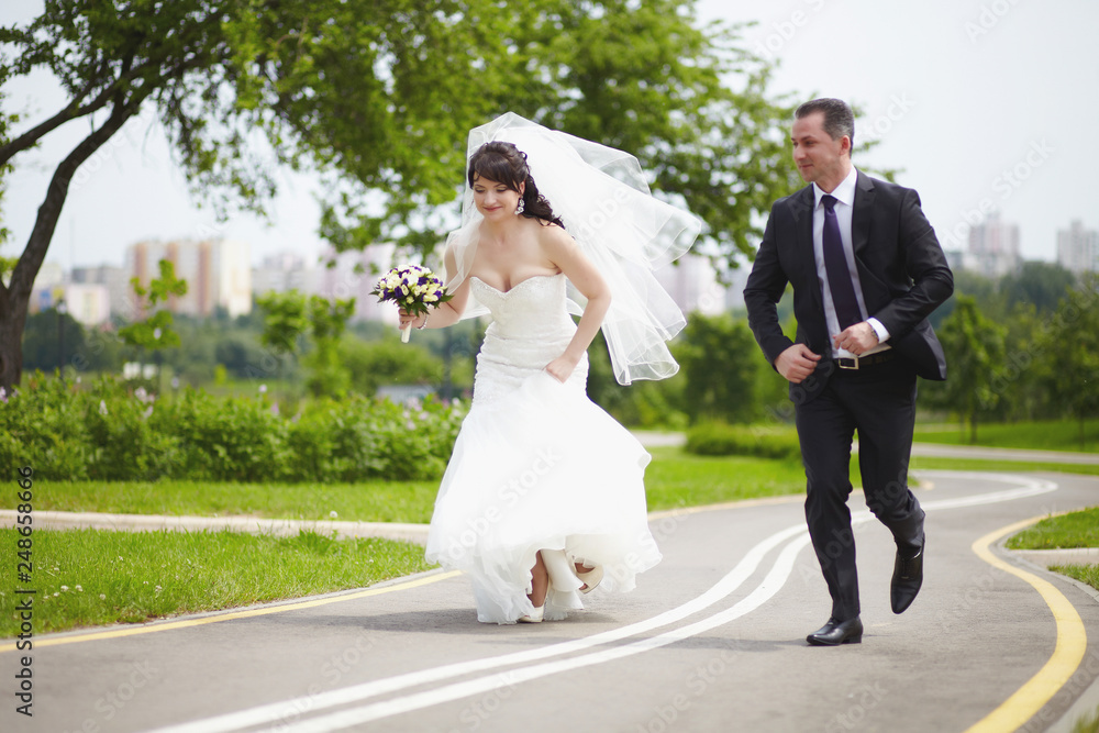 The bride and groom run together on the road in the summer The bride and groom run together on the road in the summer