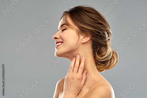 Photo beauty and people concept - smiling young woman touching her neck over grey back