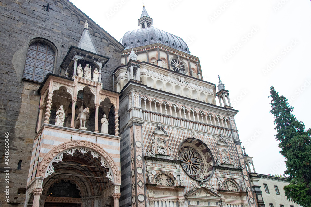 Exterior of the Basilica of St. Mary Major and the Colleoni Chapel. The front facade has a series of polychrome decorations in cream and pink tones. Piazza del Duomo in Bergamo, Italy.